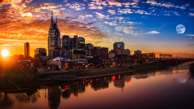 City skyline at sunset with colorful clouds, river in foreground reflecting buildings and lights